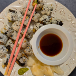 Overhead view of sushi rolls with soy sauce, wasabi, and pickled ginger with pink chopsticks over the top