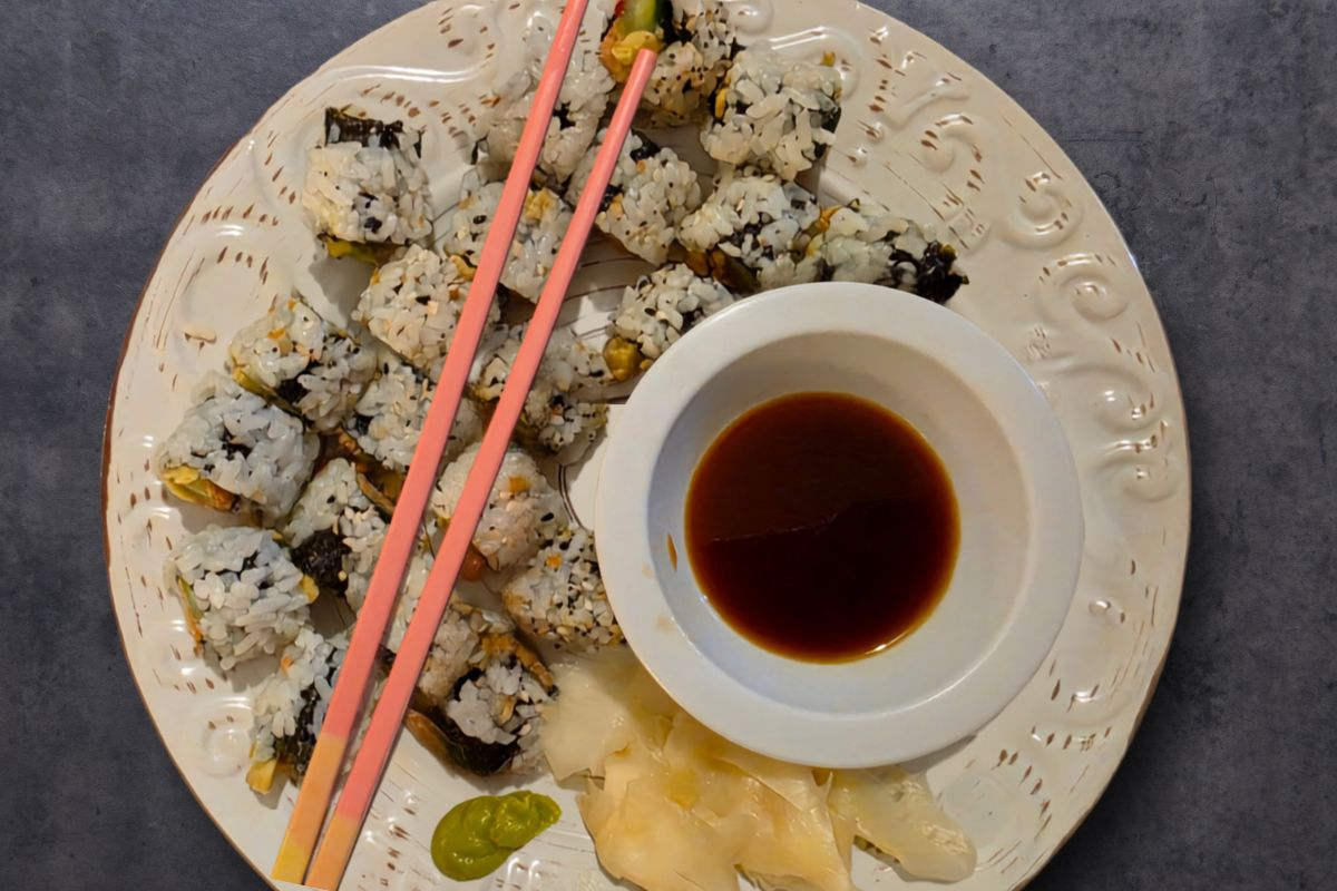 Overhead view of sushi rolls with soy sauce, wasabi, and pickled ginger with pink chopsticks over the top